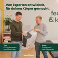 Zwei Männer packen gemeinsam eine Feder & Kern Matratze aus einem Karton in einem hellen Raum aus.