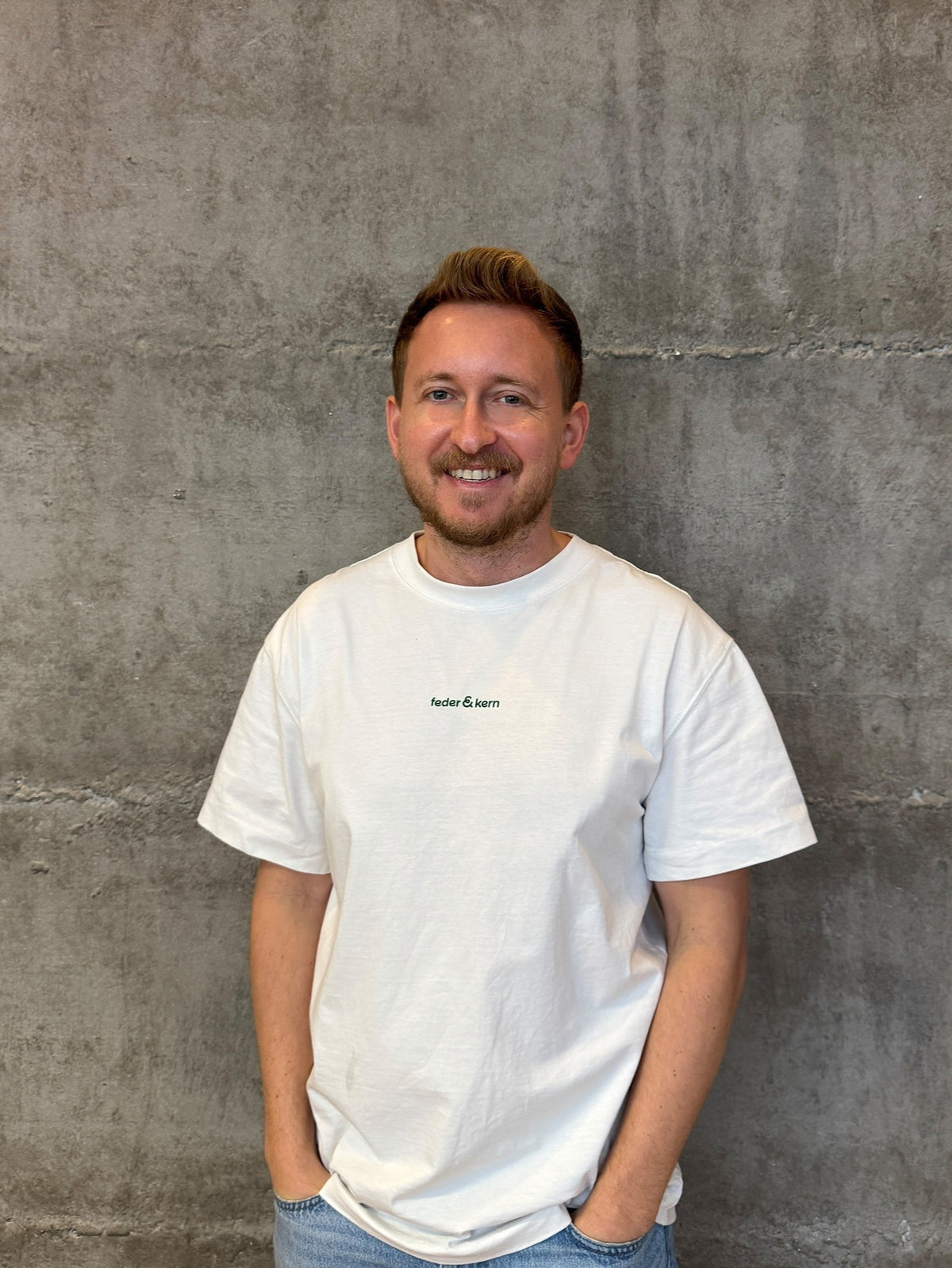 Feder & Kern Mitgründer Peter, weißes T-Shirt, vor grauer Betonwand, Schlafcoach
